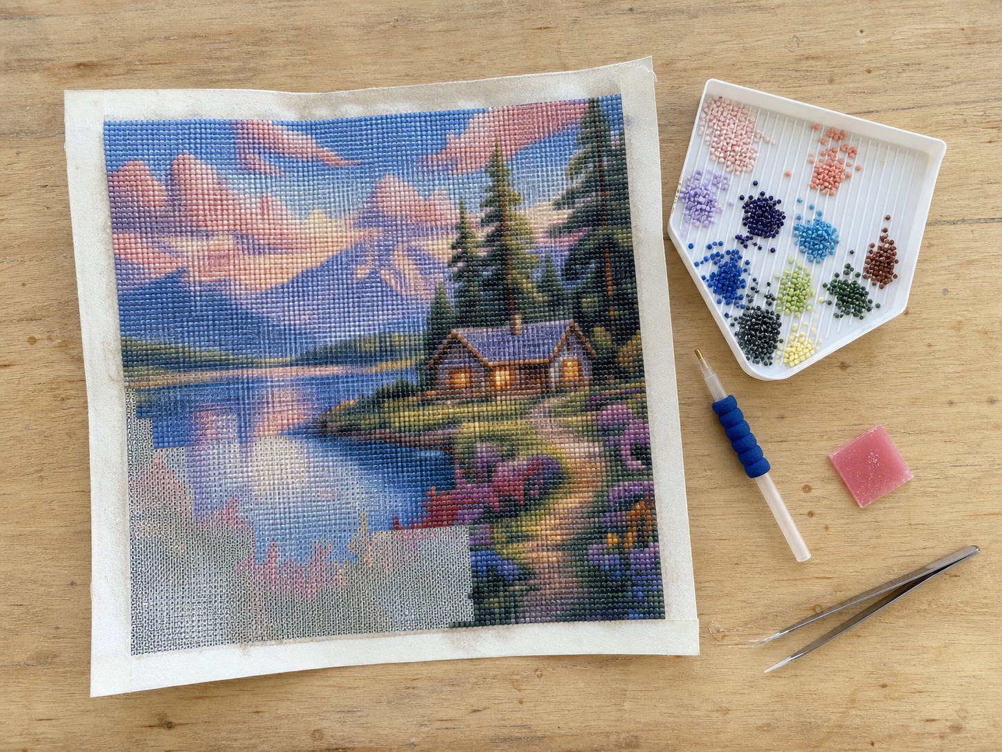 Complete diamond painting set met canvas, pen, gesorteerde steentjes, wax en pincet op een houten tafel