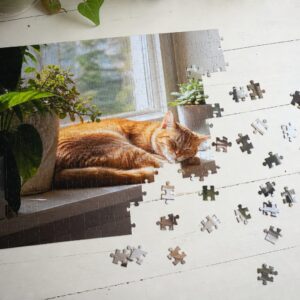 Half gelegde fotopuzzel van een rode kat op een zonnige vensterbank