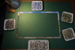 Puzzel van 1000 stukjes met alleen de rand gelegd en de stukjes op kleur gesorteerd in vijf bakjes