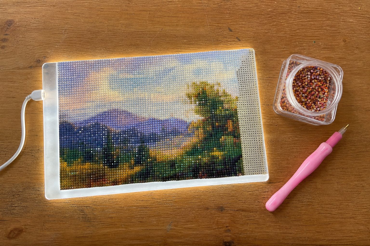 LED-lightpad met half afgewerkt diamond painting canvas, sorteerpotje met steentjes en een ergonomische roze pen op een houten bureau